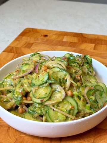 Viral cucumber salad with chickpeas, avocado, and red onion in a creamy dressing, served in a white bowl.