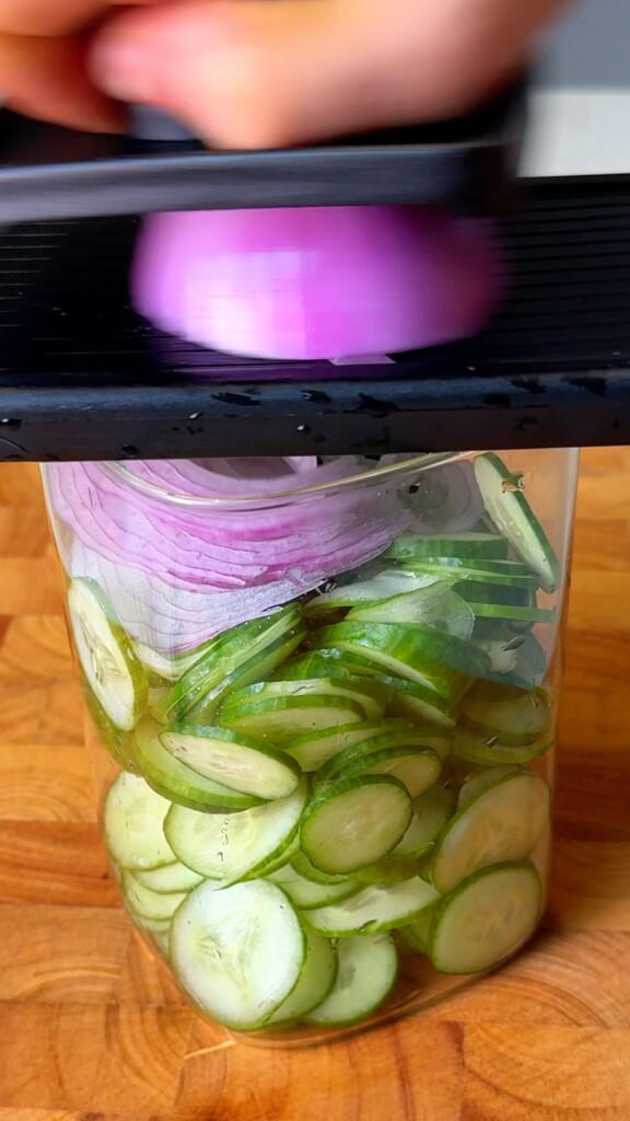Sliced red onion layered over cucumber in a glass jar
