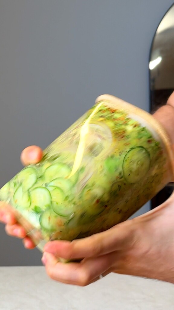 Hand shaking the sealed jar of viral cucumber salad to coat with dressing