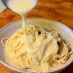 Creamy lemon sauce being ladled over a bowl of spaghetti