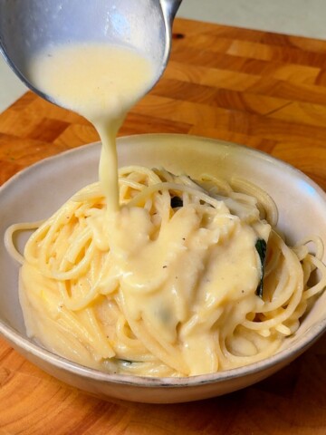 Creamy lemon sauce being ladled over a bowl of spaghetti