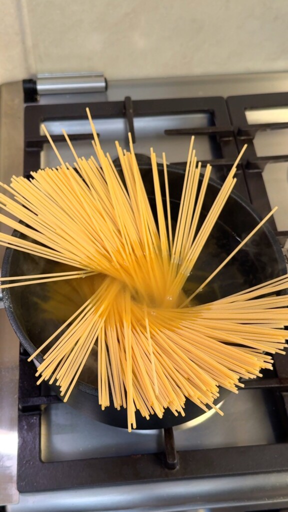 Dry spaghetti fanning out in a pot of salted boiling water on the stove