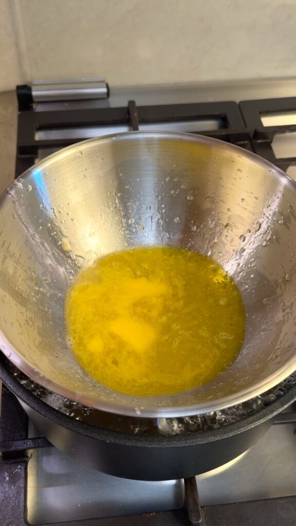 Vegan butter and olive oil melting together in a metal bowl set over a pot of boiling water