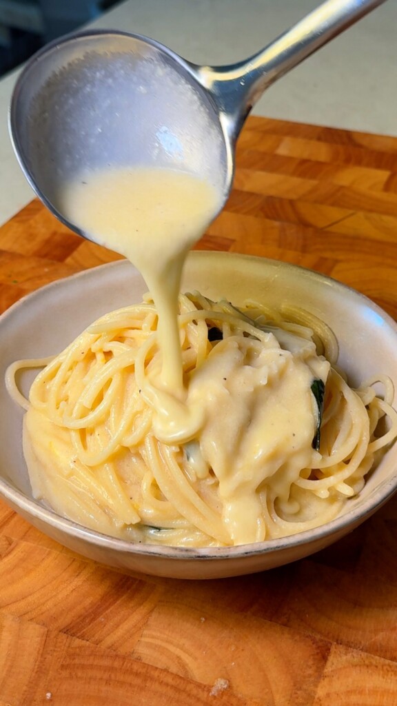 Creamy lemon sauce being ladled over a bowl of spaghetti