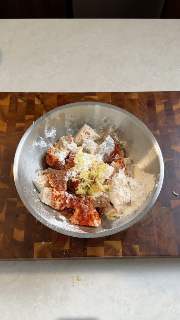 Torn tofu pieces in a metal bowl coated with cornstarch, rice flour, smoked paprika, and grated ginger for crispy gochujang tofu