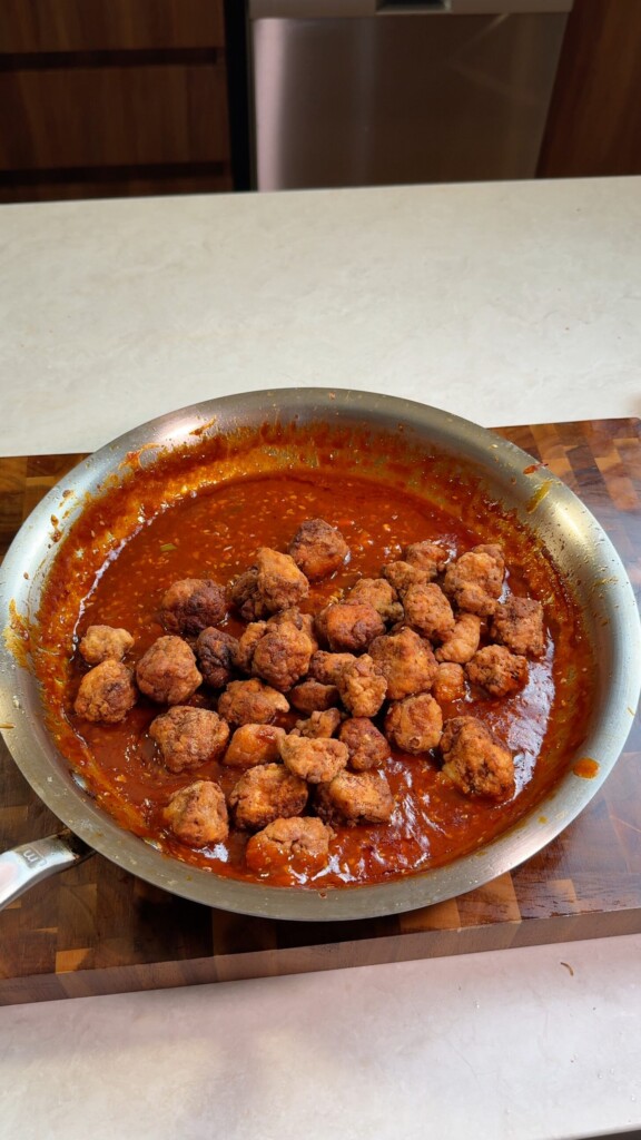 Crispy fried tofu pieces added to a pan of sticky gochujang sauce before tossing