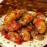 Pan fried baby potatoes served over creamy hummus and topped with chili oil and fresh herbs on a rustic plate