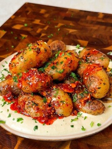 Pan fried baby potatoes served over creamy hummus and topped with chili oil and fresh herbs on a rustic plate