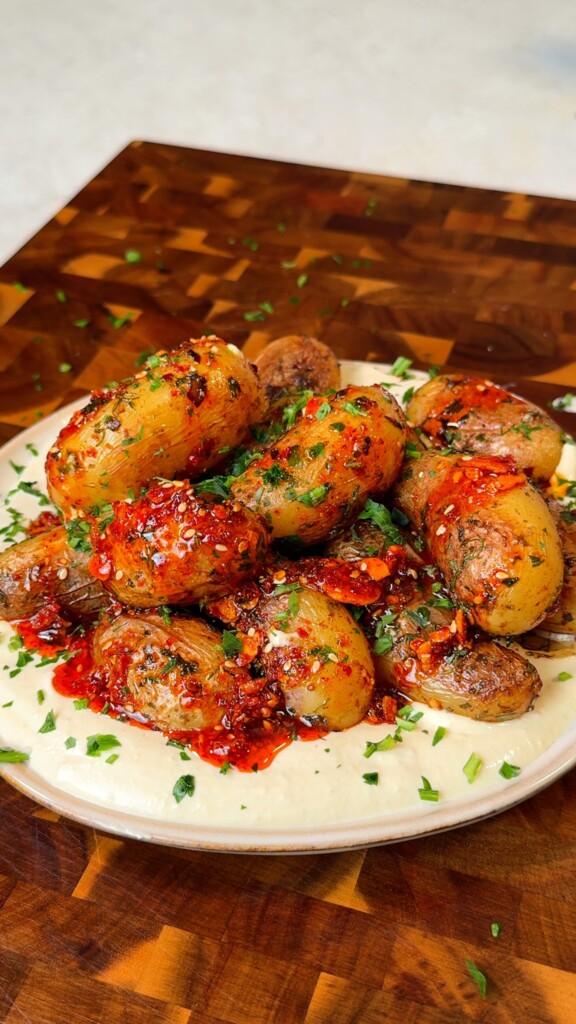 Pan fried baby potatoes served over creamy hummus and topped with chili oil and fresh herbs on a rustic plate