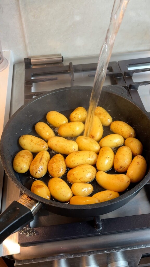 Baby potatoes in a pan with water being poured in to simmer until tender for pan fried baby potatoes