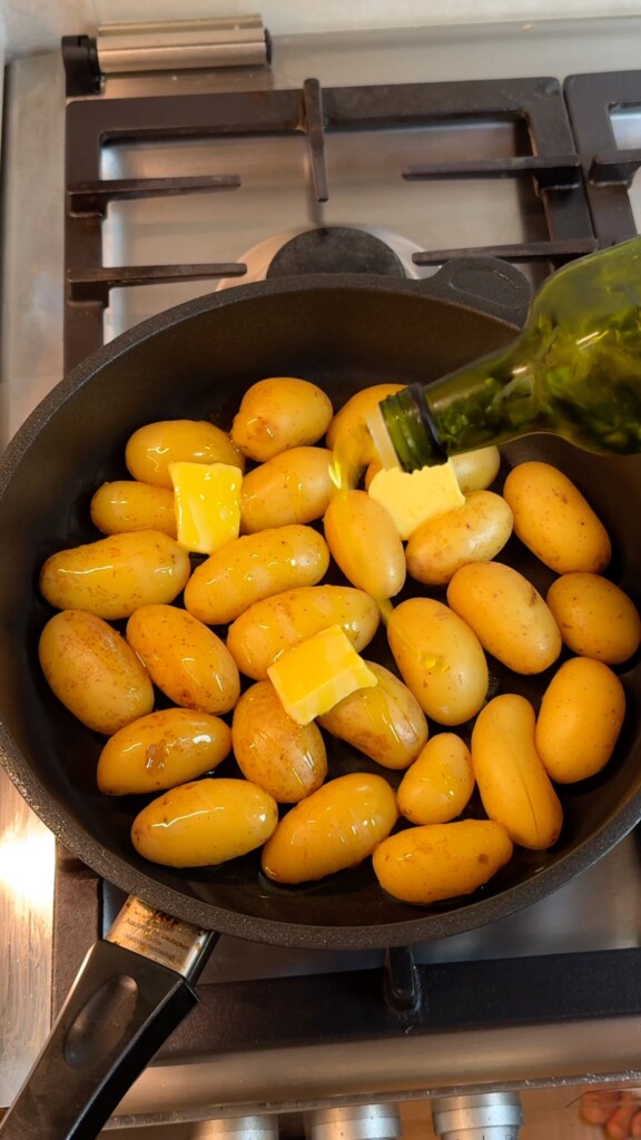 Baby potatoes in a pan with vegan butter and olive oil added after simmering, ready to be pan fried