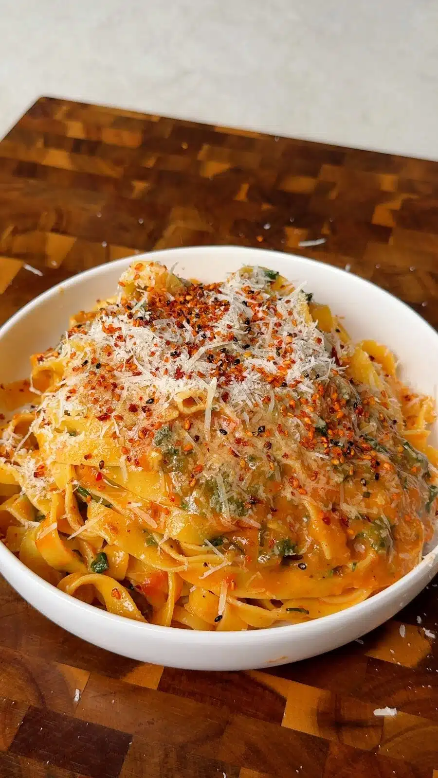 Creamy zucchini pasta in a bowl topped with vegan parmesan and chili flakes