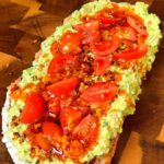 Pea pesto toast on sourdough topped with cherry tomatoes, sesame seeds, and chili oil
