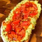 Pea pesto toast on sourdough topped with cherry tomatoes, sesame seeds, and chili oil