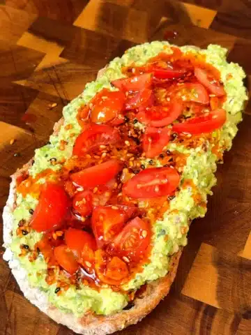 Pea pesto toast on sourdough topped with cherry tomatoes, sesame seeds, and chili oil