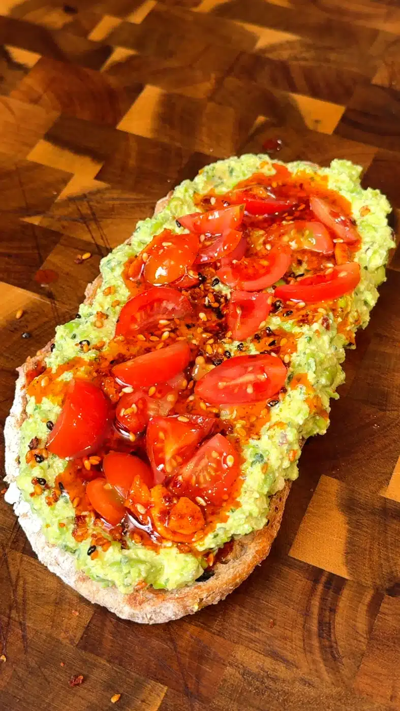 Pea pesto toast on sourdough topped with cherry tomatoes, sesame seeds, and chili oil