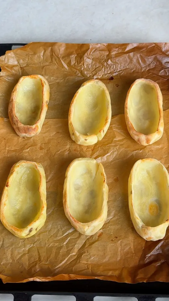 Baked potato boats hollowed into shells on a parchment lined tray for vegan loaded baked potatoes