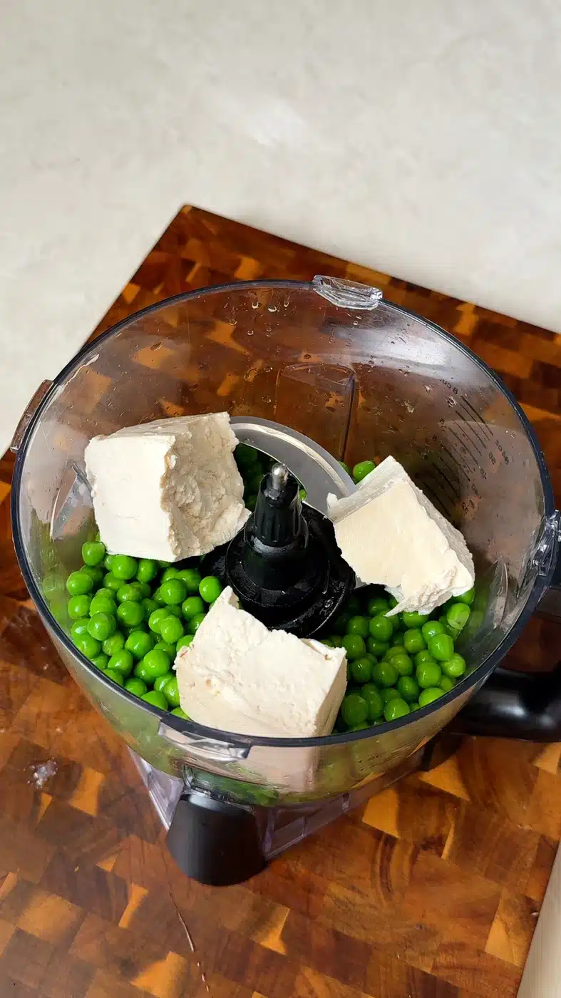 Green peas and firm tofu chunks in a food processor for pea pesto