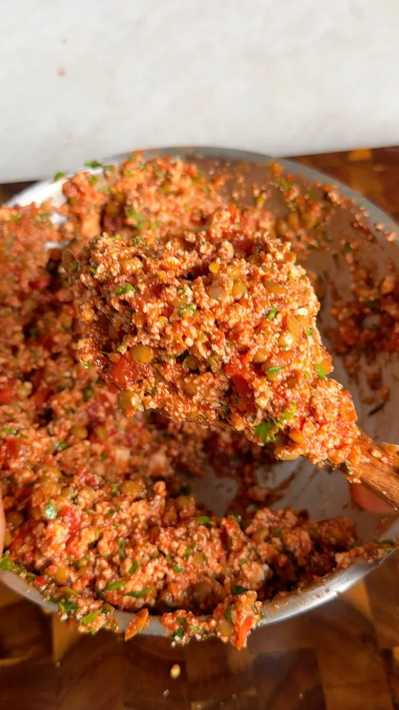 Spiced lentil and tofu filling with tomato and parsley on a wooden spoon over a metal bowl