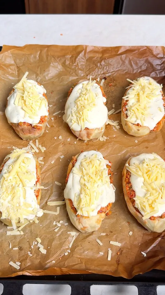 Vegan loaded baked potatoes topped with dairy free béchamel and grated vegan cheese before baking