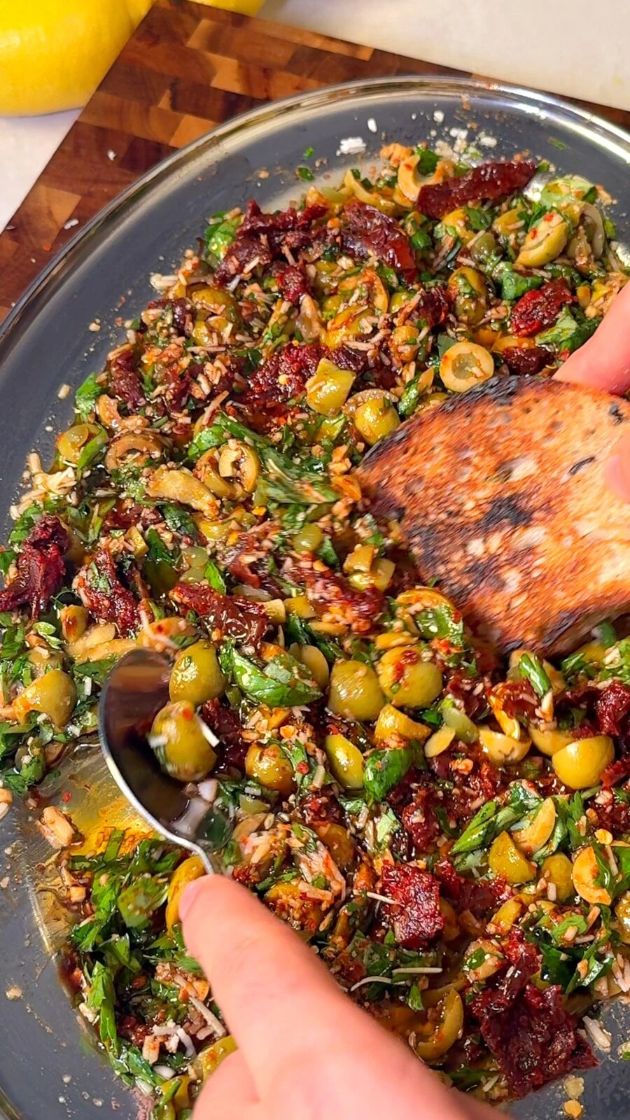 Spooning olive bruschetta topping onto charred sourdough