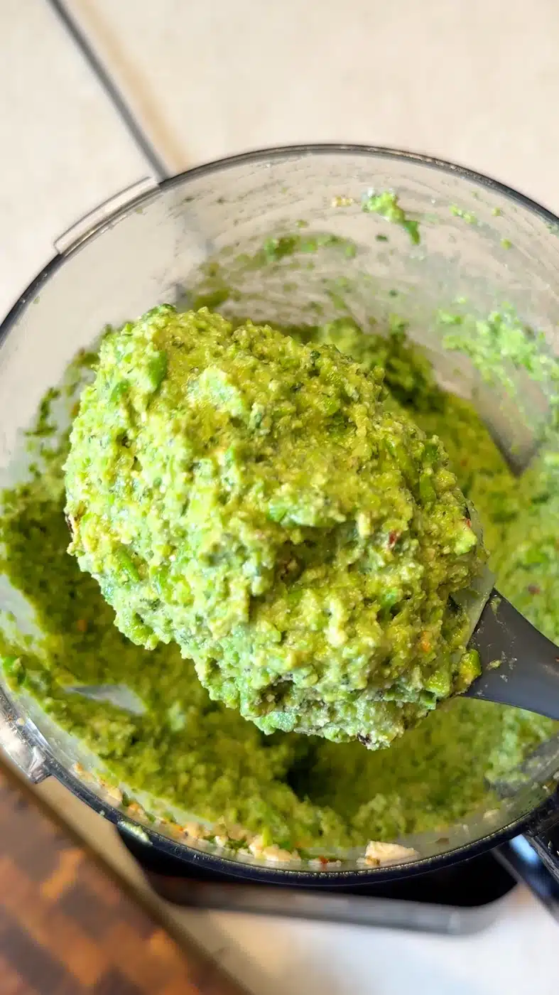 Thick and creamy pea pesto with tofu and mint on a spatula over the food processor