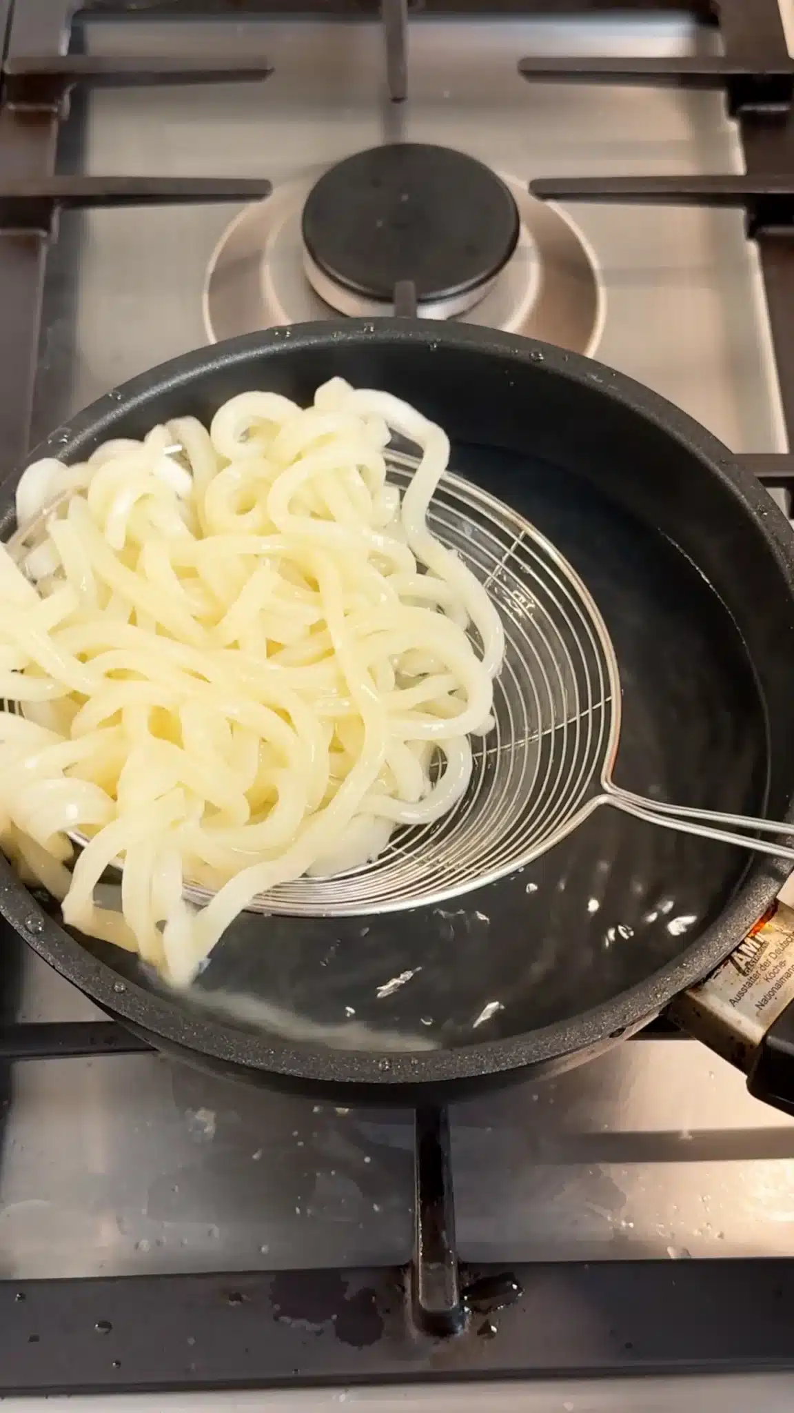 Cooked udon noodles being lifted from a pot with a strainer