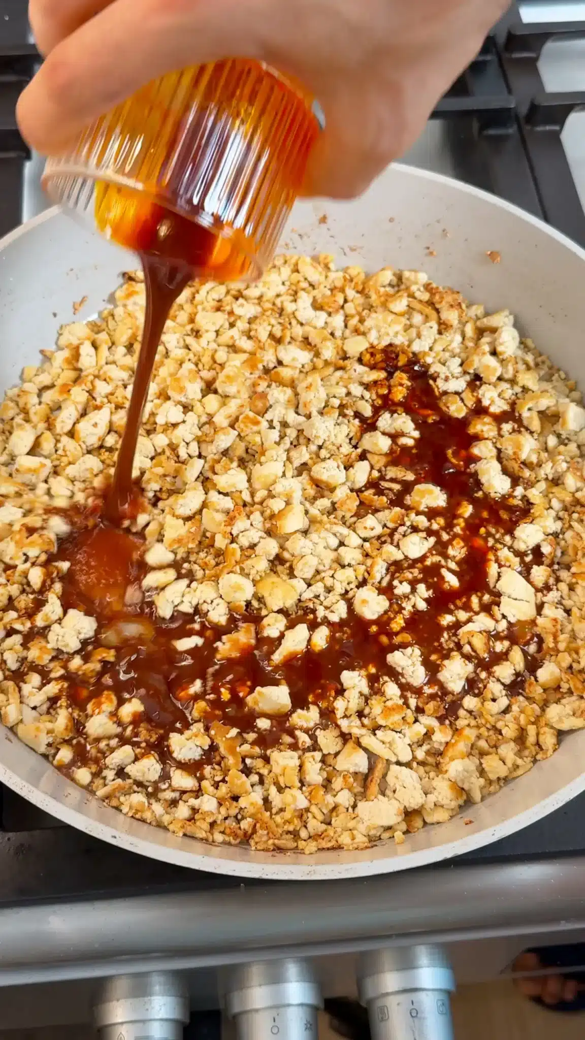 Dark soy glaze being poured over browned tofu crumbles