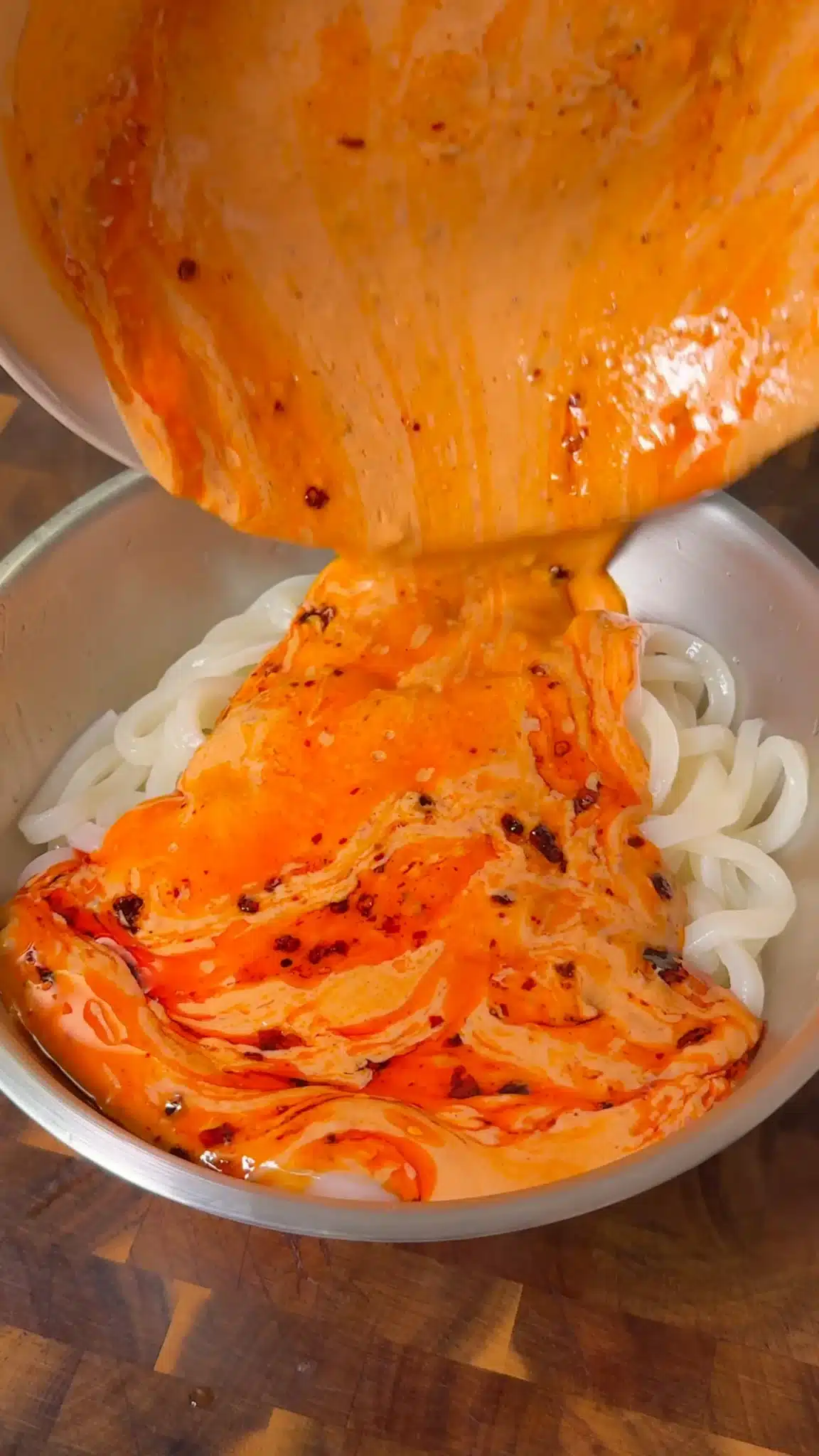 Creamy orange tofu sauce being poured over cooked udon noodles