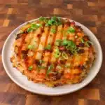 Golden rice paper sandwich with grill marks, sliced spring onion and chili garnish on a pale plate