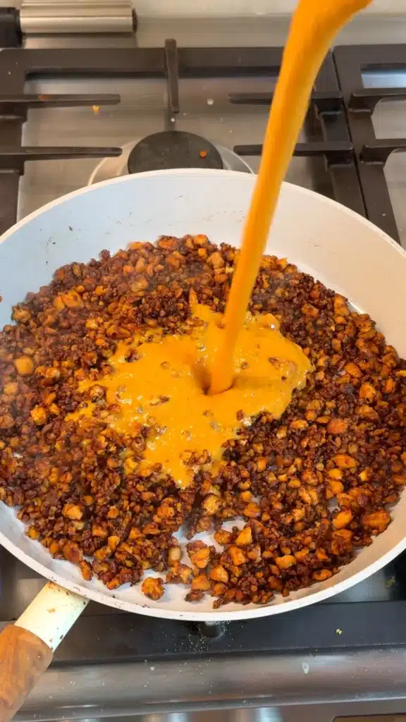 Roasted red pepper sauce being poured over browned tofu crumbles