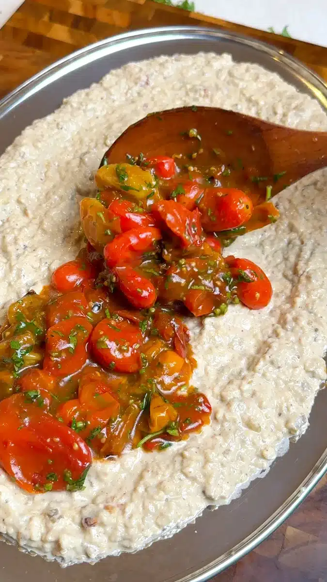 Roasted cherry tomatoes being spooned over a textured eggplant tahini dip