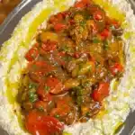 Creamy eggplant dip topped with balsamic cherry tomatoes, parsley and olive oil on a metal platter