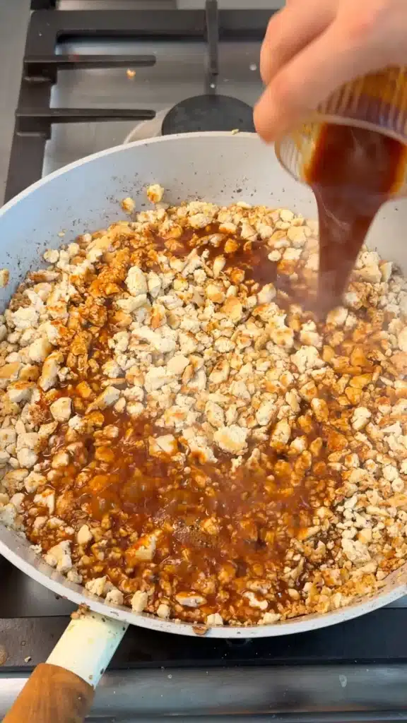 Soy sauce seasoning being poured over tofu crumbles