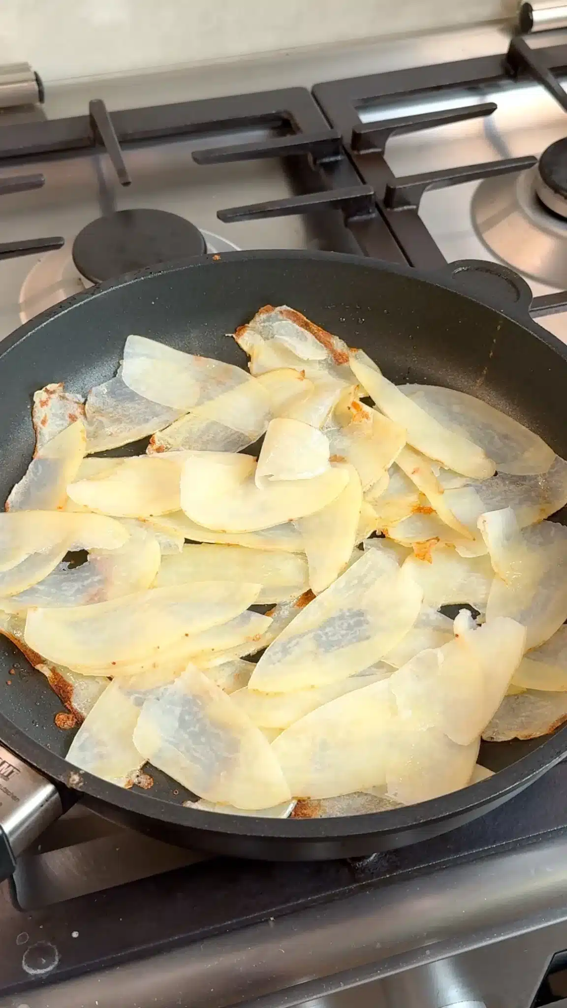 Thin overlapping potato slices cooking in a nonstick frying pan