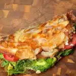 Golden skillet potato wrap filled with avocado, tomato, greens and tofu on a wooden board