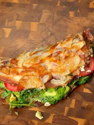 Golden skillet potato wrap filled with avocado, tomato, greens and tofu on a wooden board