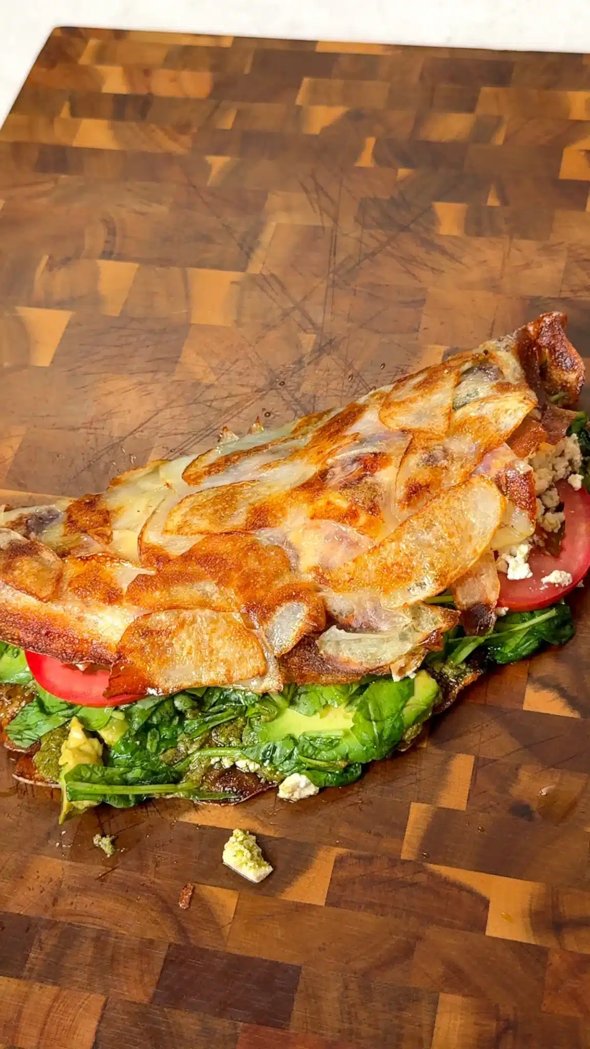 Golden skillet potato wrap filled with avocado, tomato, greens and tofu on a wooden board