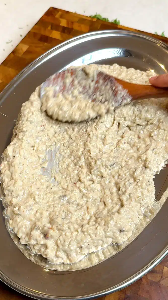Creamy eggplant mixture being spread across a metal platter with a wooden spoon