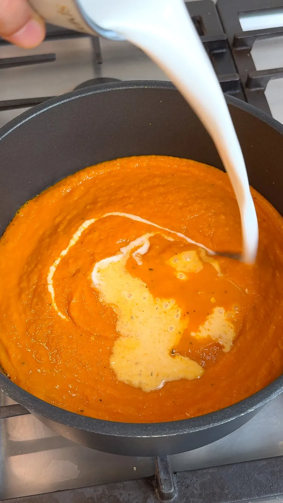 Coconut milk being poured into blended butternut squash soup in a pot