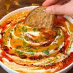 Sourdough bread dipped into a bowl of vegan roasted butternut squash soup with coconut milk and chili oil swirl