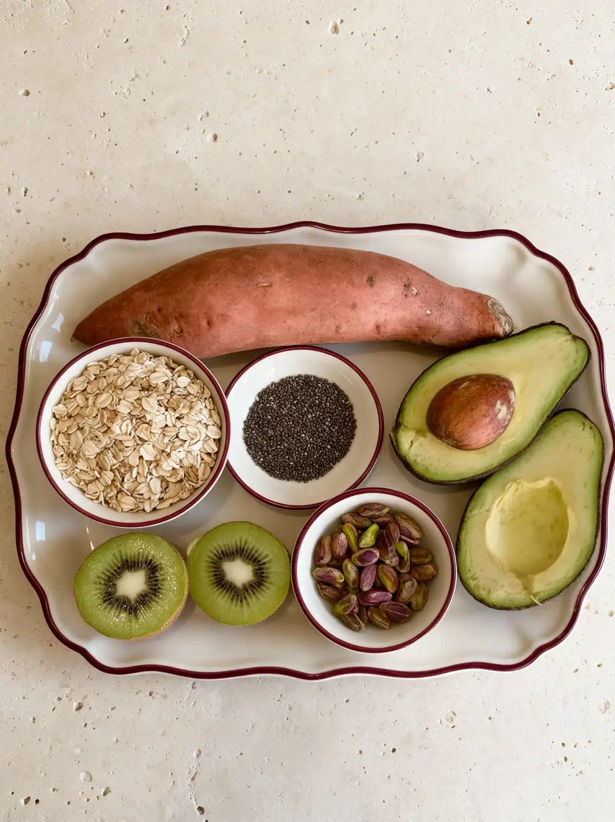 Sweet potato, rolled oats, chia seeds, avocado, green kiwi and pistachios arranged on an ivory platter