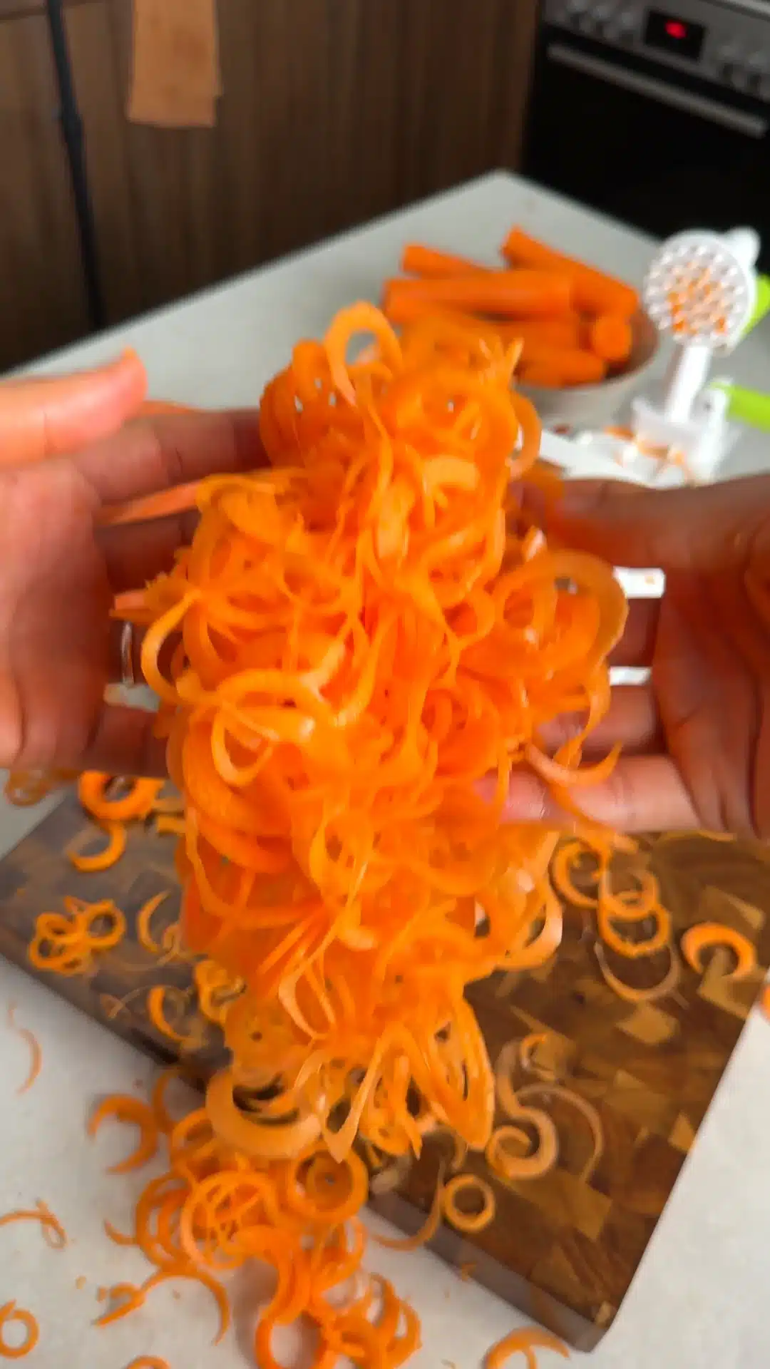 Fresh orange carrot noodles held beside a spiralizer.