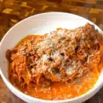 A bowl of carrot noodles with tomato tofu Bolognese and grated vegan Parmesan.