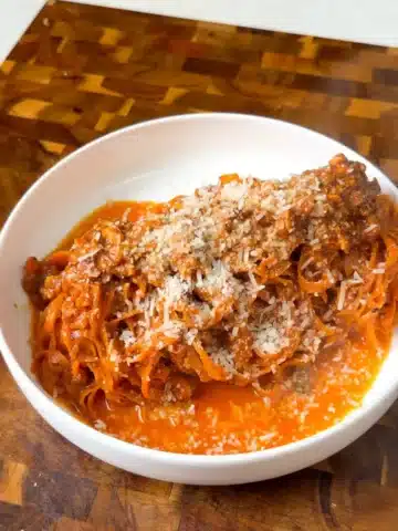 A bowl of carrot noodles with tomato tofu Bolognese and grated vegan Parmesan.
