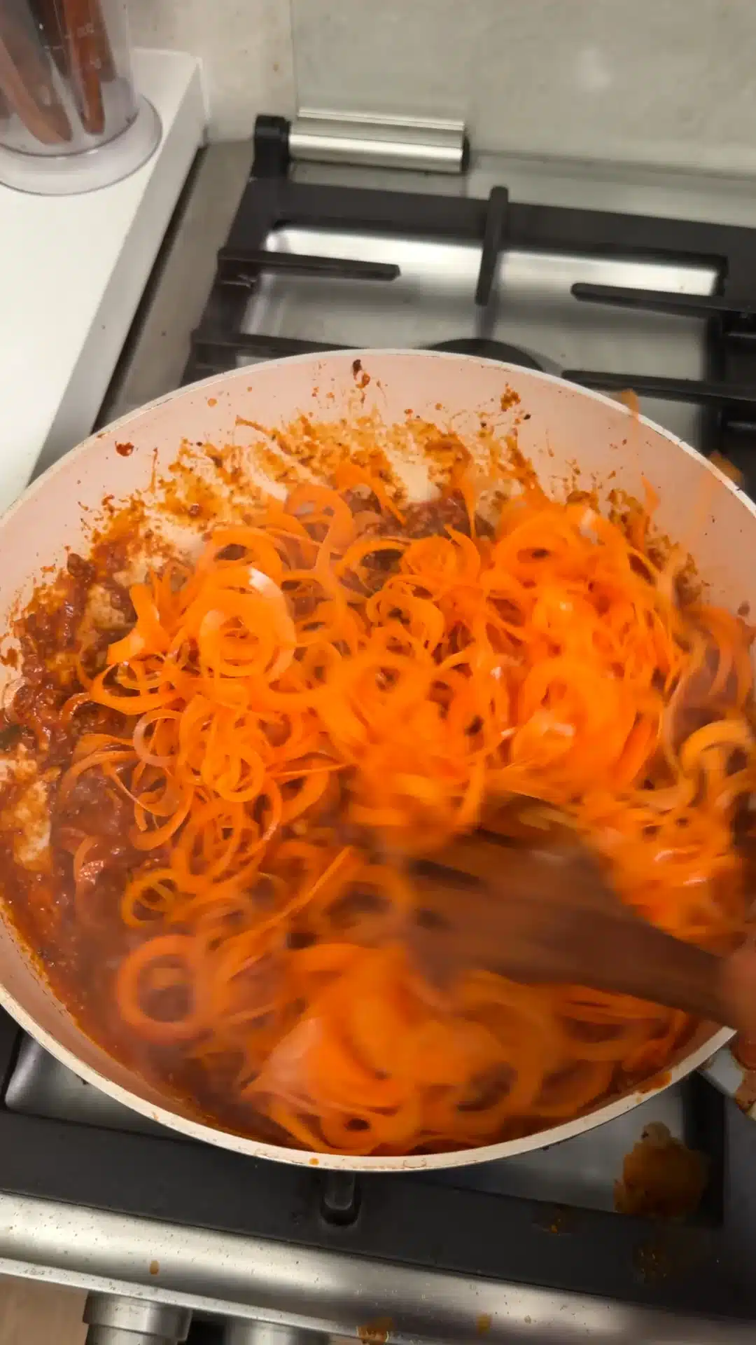 Spiralized carrots being combined with tofu Bolognese in a frying pan.