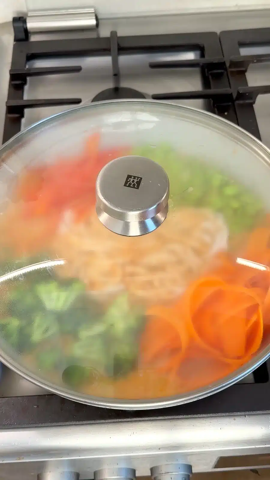 Noodles and vegetables cooking under a glass lid