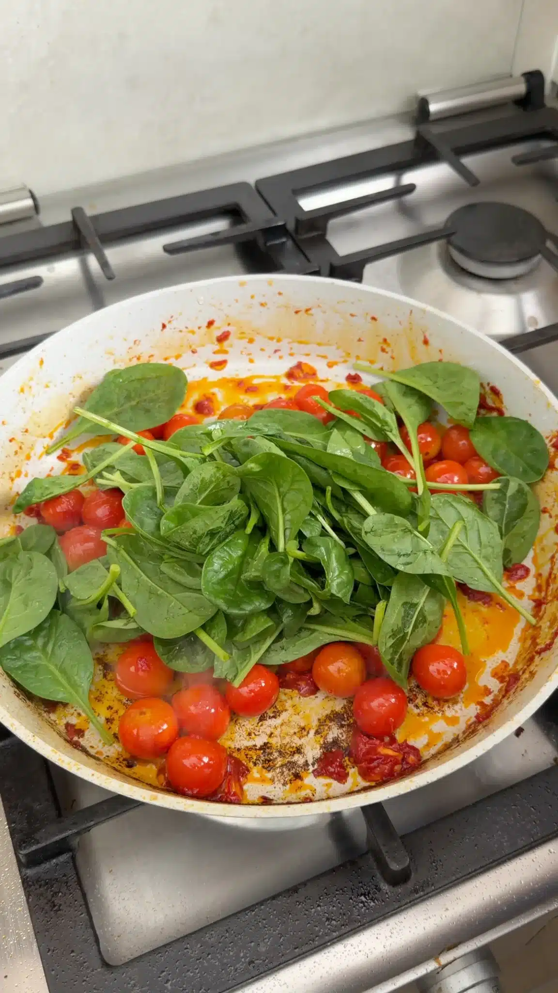 Baby spinach added to cherry tomatoes in a frying pan