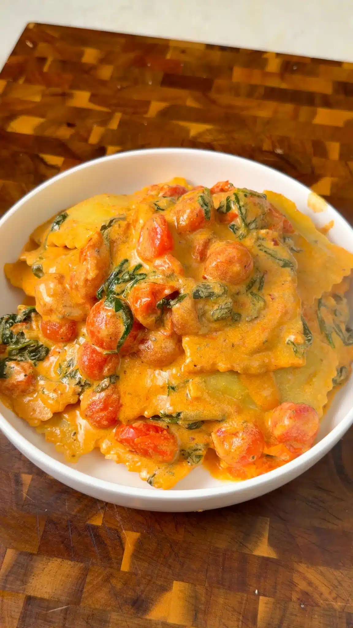 Creamy vegan ravioli with cherry tomatoes and spinach in a white bowl