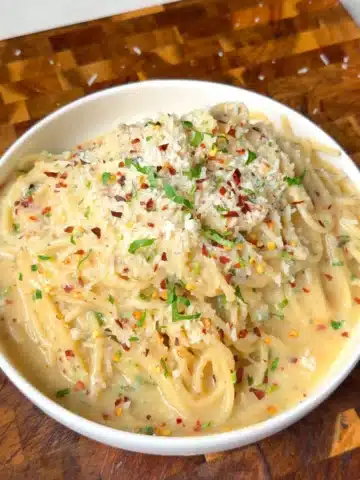 Creamy garlic confit butter pasta with vegan Parmesan, parsley and chili flakes in a white bowl